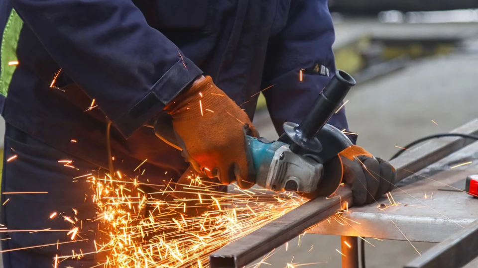 Soudeur professionnel travaillant dans un atelier industriel, portant un masque de protection et manipulant un chalumeau produisant des étincelles intenses sur une pièce métallique